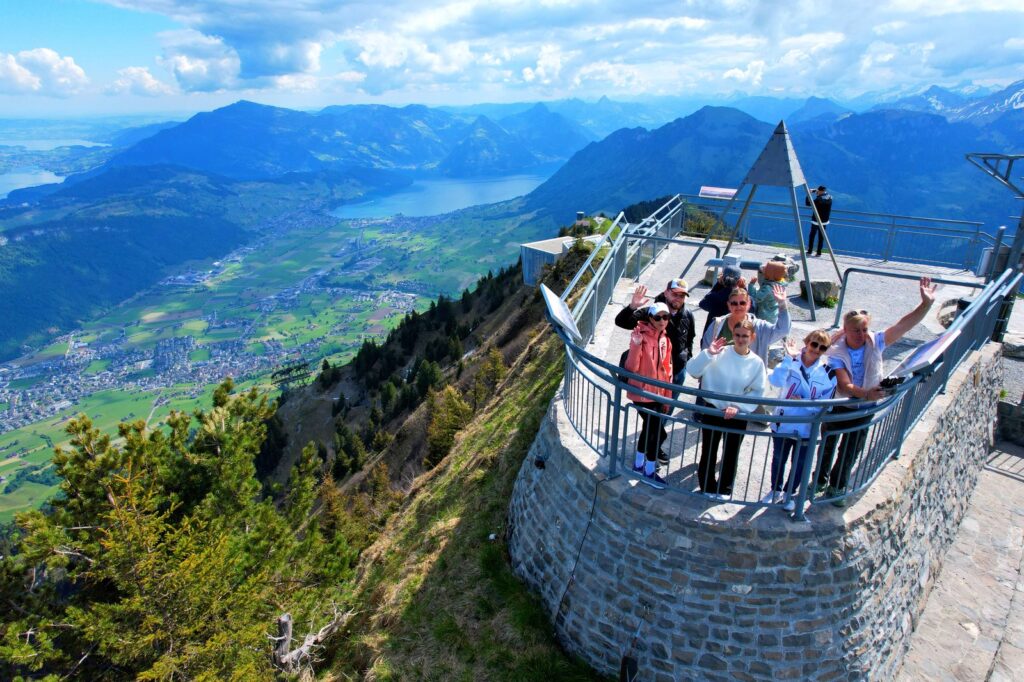Tourists waving at a drone camera from a circular viewing platform in the Swiss Alps — a unique photo opportunity on a private tour