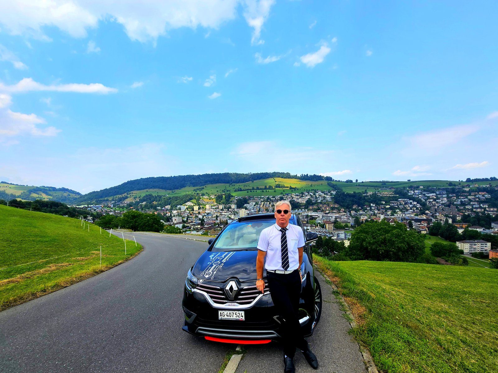 専用車 Renault Espace Initiale の横に立つガイドのTuri。スイスの丘の上、町を見下ろす道で撮影。