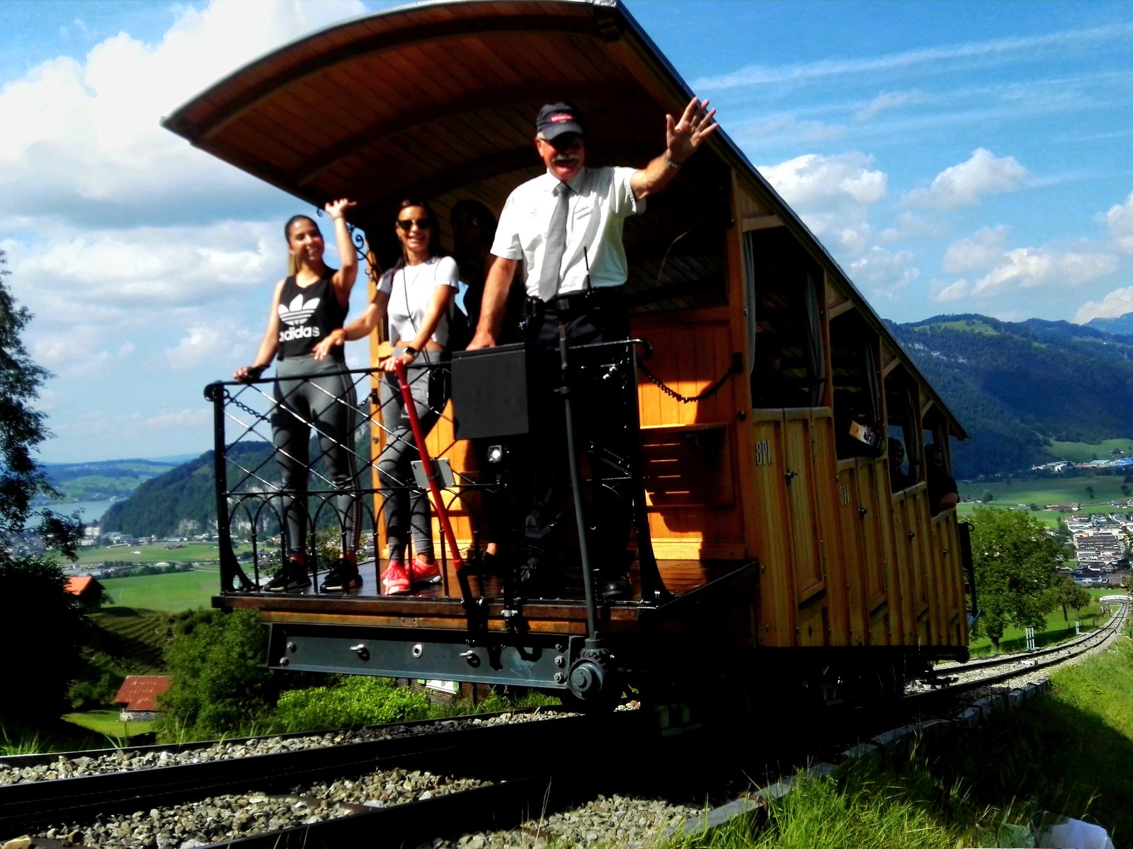 スイスの登山鉄道のオープンデッキ車両。車掌と乗客が外の景色を眺めている